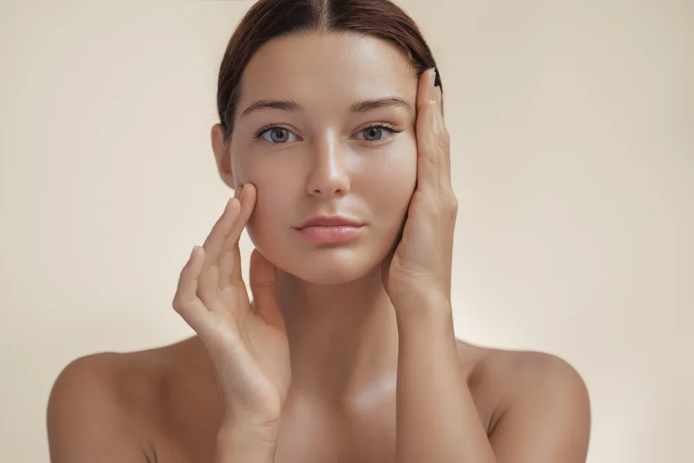 Woman with hands on her cheeks looking directly at camera with clear skin