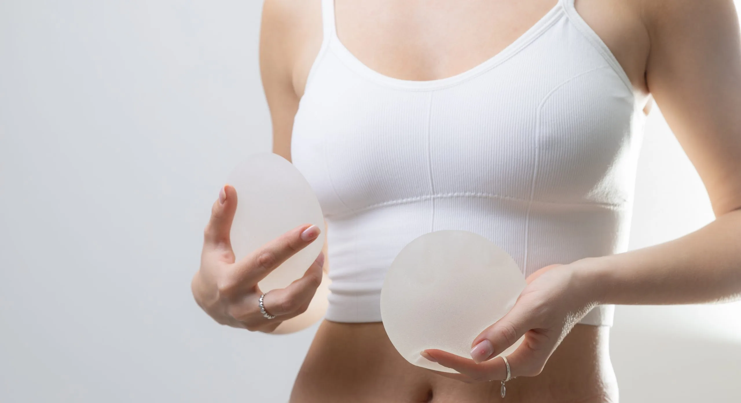 Woman in white sports bra holding silicone breast implant samples in both hands