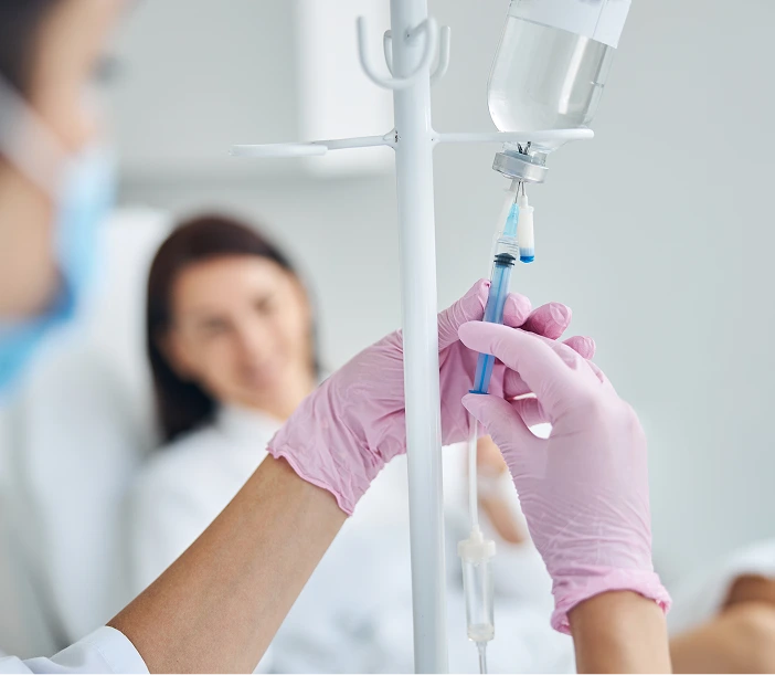 Healthcare provider in pink gloves adjusting an IV drip bag on a medical stand