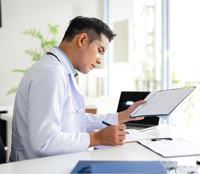 Doctor in white coat reviewing patient chart at desk with laptop