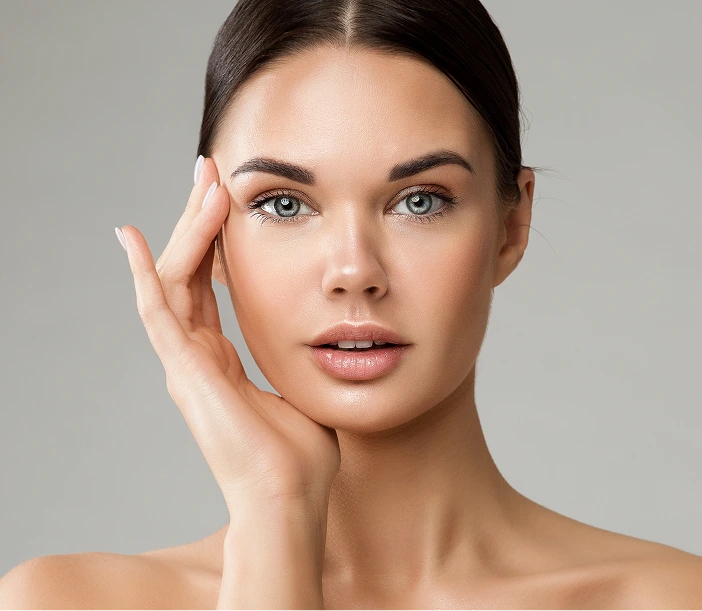 Woman with glowing skin touching her face against gray background