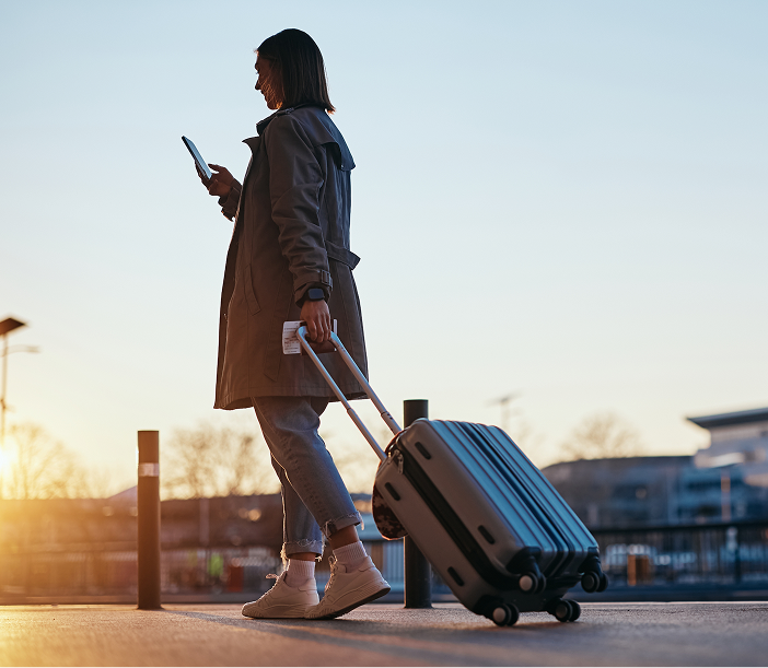 Woman holding phone and luggage at airport at sunset