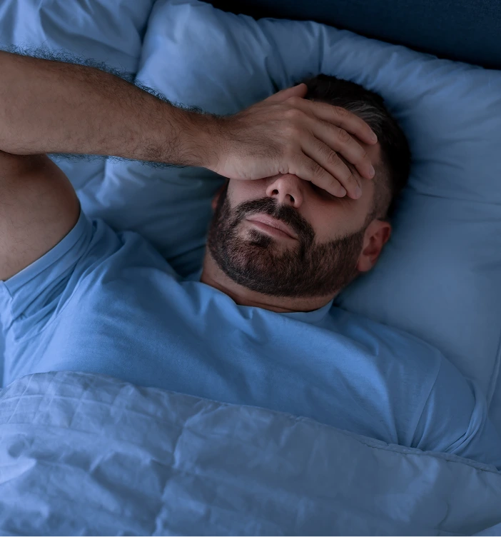 Man lying in bed covering face with hand