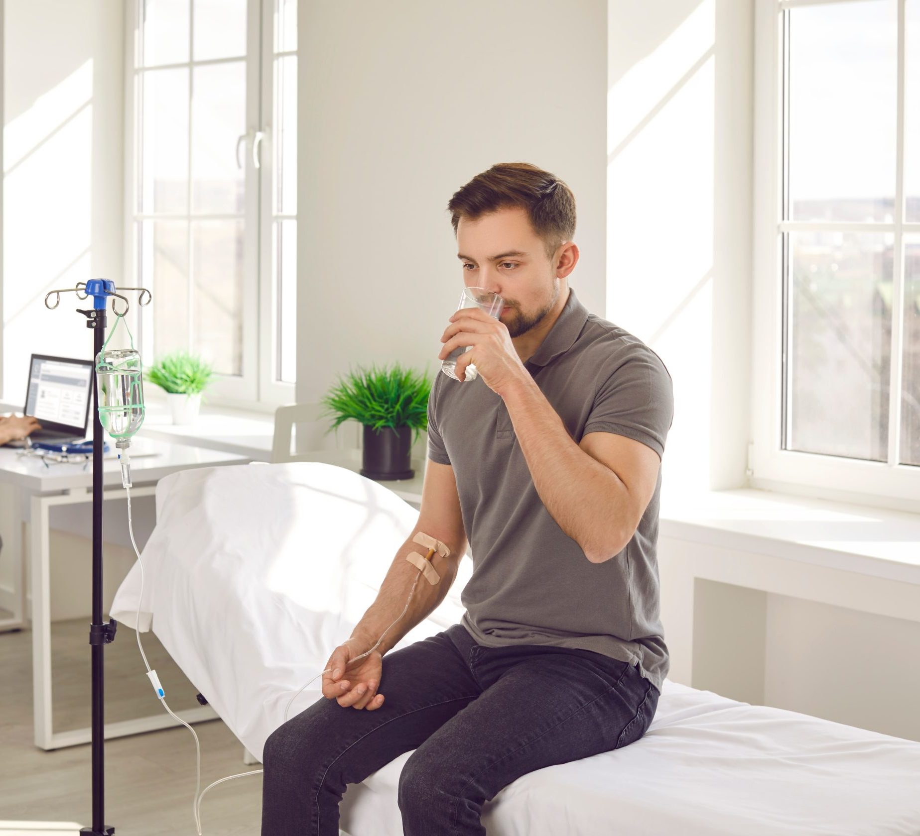 Man receiving IV therapy in bright medical office, holding gauze on his arm near IV stand