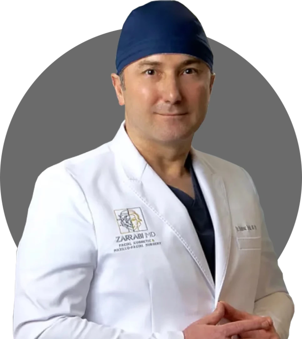 Male surgeon wearing white coat with Zarrabi MD logo and surgical cap